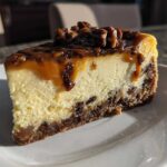 A decadent slice of turtle cheesecake featuring a creamy filling, dark crust, dripping caramel, and pecan topping.