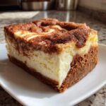 A close-up, tempting slice of snickerdoodle cheesecake featuring a creamy white center and a cinnamon-swirled, dark brown top.