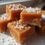A stack of soft, chewy caramels topped generously with flaky sea salt crystals.