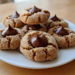 A close-up of several soft and chewy peanut butter blossoms rolled in sugar, each topped with a chocolate kiss.