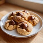 A close-up of several soft peanut butter blossoms cookies rolled in sugar, each topped with a chocolate kiss.