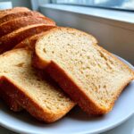 Close-up of soft, evenly sliced sourdough sandwich bread on a white plate.