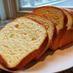 Four thick slices of soft, golden sourdough sandwich bread displayed on a light plate.