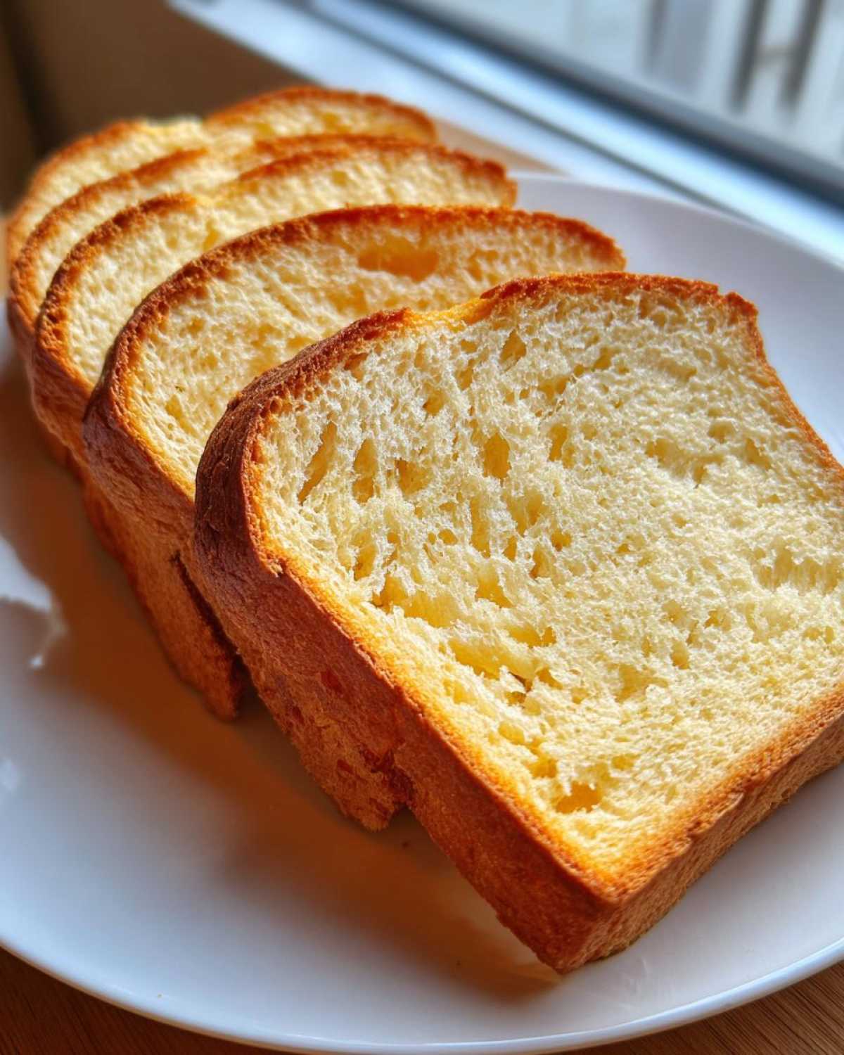 Four golden-brown slices of soft sourdough sandwich bread displayed on a white plate.