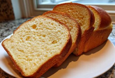 Four thick slices of soft, golden sourdough sandwich bread displayed on a light plate.