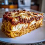 A thick, layered slice of baked spaghetti pie topped with meat sauce and melted mozzarella cheese.