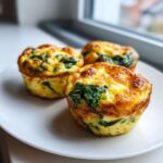 Three golden brown spinach egg muffin bites served on a white plate near a window.