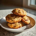 A stack of four golden brown butter pecan cookies resting on a light gray plate, illuminated by natural sunlight.