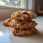 A stack of three chewy almond joy cookies showing oats, coconut, and chocolate chips.