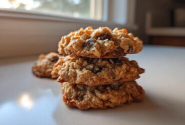 A stack of three chewy almond joy cookies showing oats, coconut, and chocolate chips.