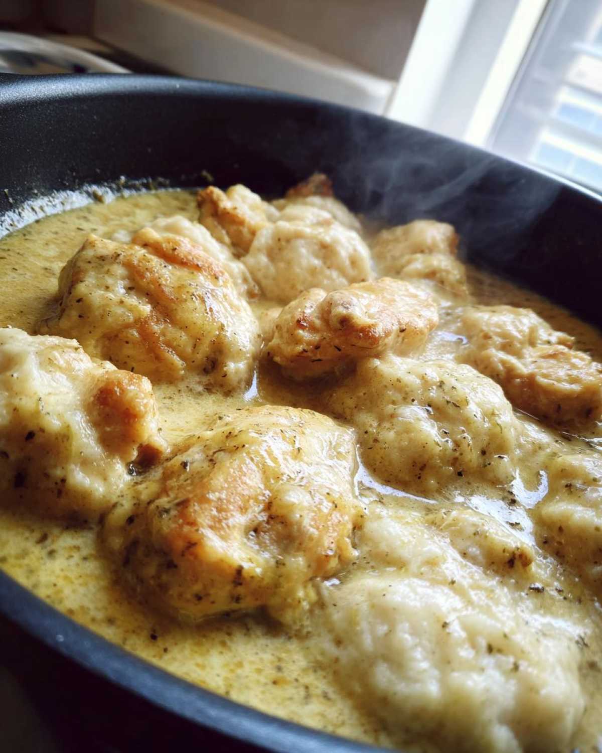 Close-up of fluffy dumplings simmering in a creamy sauce for chicken and dumplings recipe.