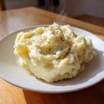A generous serving of fluffy, steaming slow cooker mashed potatoes topped with melted butter and dried herbs.