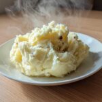 A generous serving of fluffy, steaming slow cooker mashed potatoes with bits of skin visible, served on a white plate.