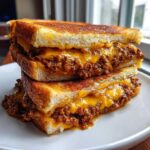 Close-up of two halves of a texas toast sloppy joes sandwich stacked, overflowing with meaty filling and melted cheddar cheese.