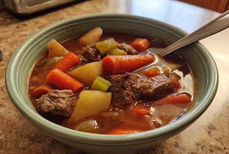Close-up of a bowl of rich vegetable beef soup, featuring chunks of beef, carrots, potatoes, and celery.