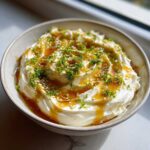 A creamy bowl of whipped feta dip drizzled with honey, topped with fresh parsley and sesame seeds.