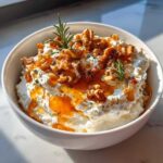 Close-up of a bowl of creamy whipped ricotta dip topped with walnuts, honey drizzle, and rosemary sprigs.