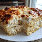 A thick, square slice of white sauce chicken lasagna with perfectly browned, bubbly cheese topping.