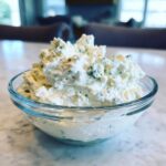 A close-up of chunky, creamy blue cheese dip served in a clear glass bowl on a marble surface.