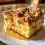 A close-up of a square serving of moist baked french toast topped with cinnamon streusel and drizzled with maple syrup.
