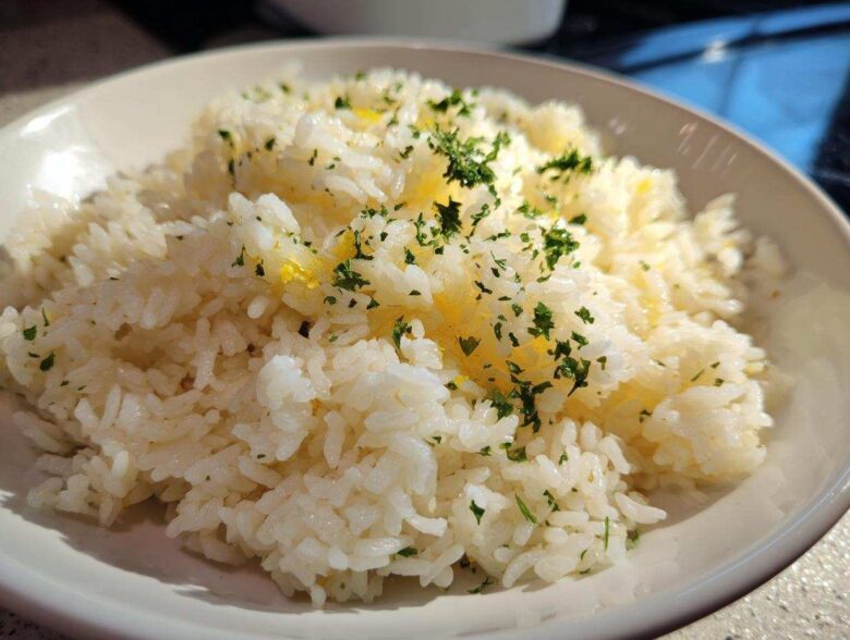 Close-up of fluffy white rice seasoned with melted butter and topped with fresh chopped parsley, showcasing the amazing butter rice flavor.
