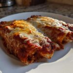 Close-up of two rolled cheese enchiladas covered in rich red sauce and melted, bubbly cheese.