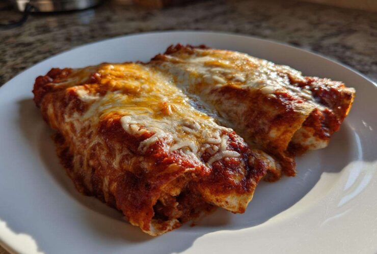 Close-up of two rolled cheese enchiladas covered in rich red sauce and melted, bubbly cheese.