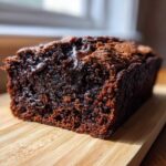 A close-up of a freshly baked, dark brown chocolate bread loaf showing a moist crumb and melted chocolate chunks.
