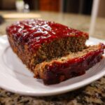 Close-up of a thick slice of homemade meatloaf topped with a shiny, thick ketchup glaze.