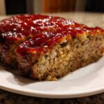 A thick slice cut from a perfectly baked meatloaf topped with a shiny, rich red glaze.