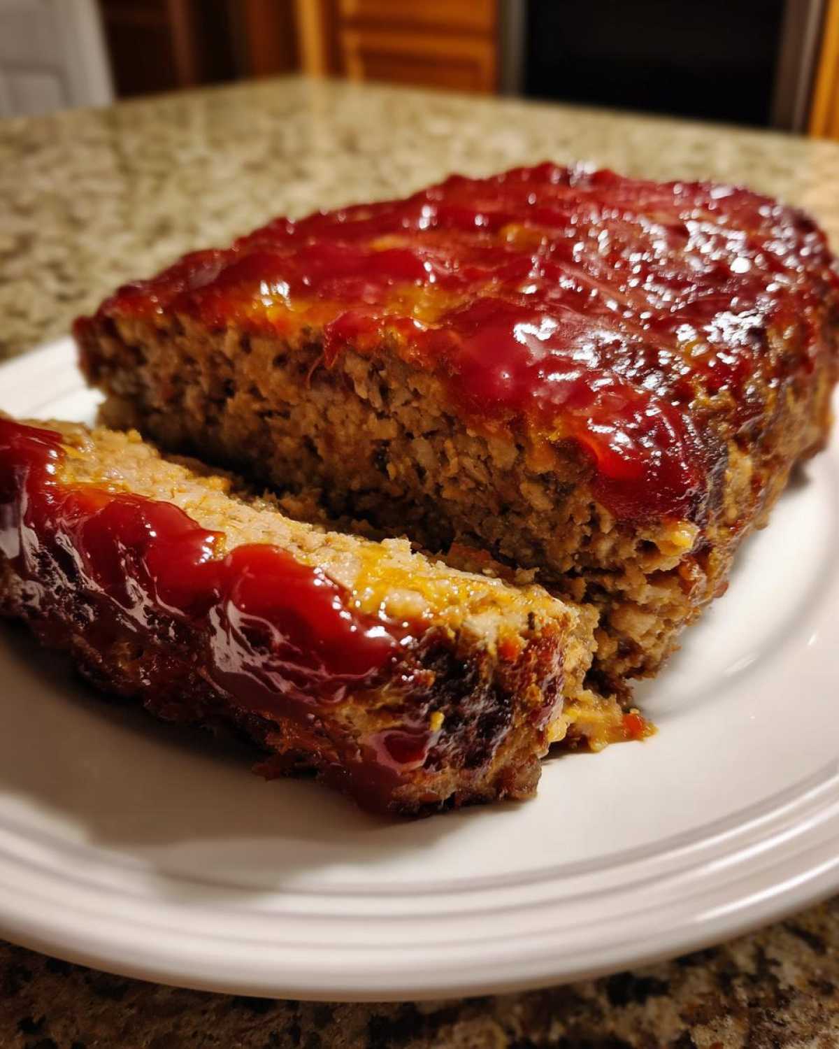 Close-up of a thick slice cut from a glazed meatloaf resting on a white plate.
