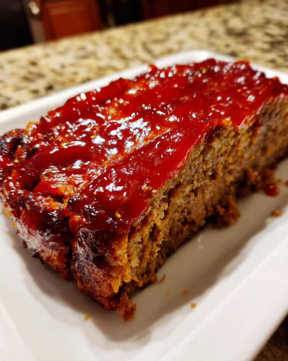 Close-up of a thick slice of moist meatloaf topped with a shiny, bright red glaze.