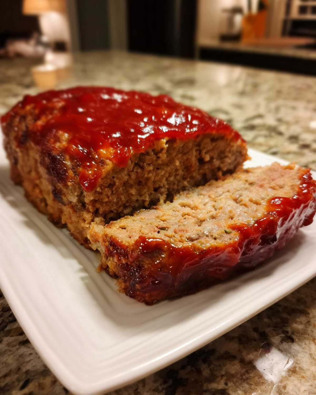 Close-up of a perfectly baked meatloaf with a thick, glossy ketchup glaze, showing one slice cut away.