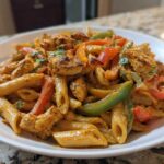 A close-up serving of creamy Rasta pasta mixed with seasoned chicken pieces and colorful bell peppers.