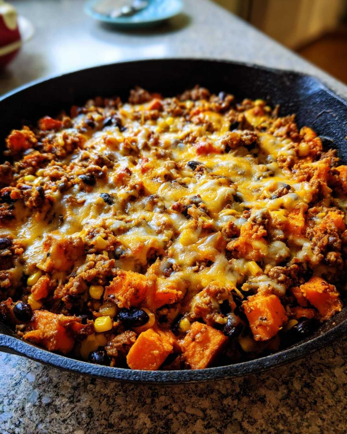 Close-up of a savory sweet potato skillet topped with melted cheese, ground meat, black beans, and corn.