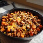 Close-up of a savory sweet potato skillet with ground meat, black beans, corn, and melted cheddar cheese.