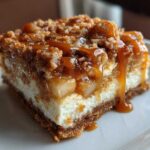 Close-up of a rich apple cheesecake bars square topped with crumble and drizzled with thick caramel sauce.