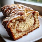 A close-up view of a slice cut from a loaf of apple fritter bread, showing cinnamon swirl and vanilla glaze.