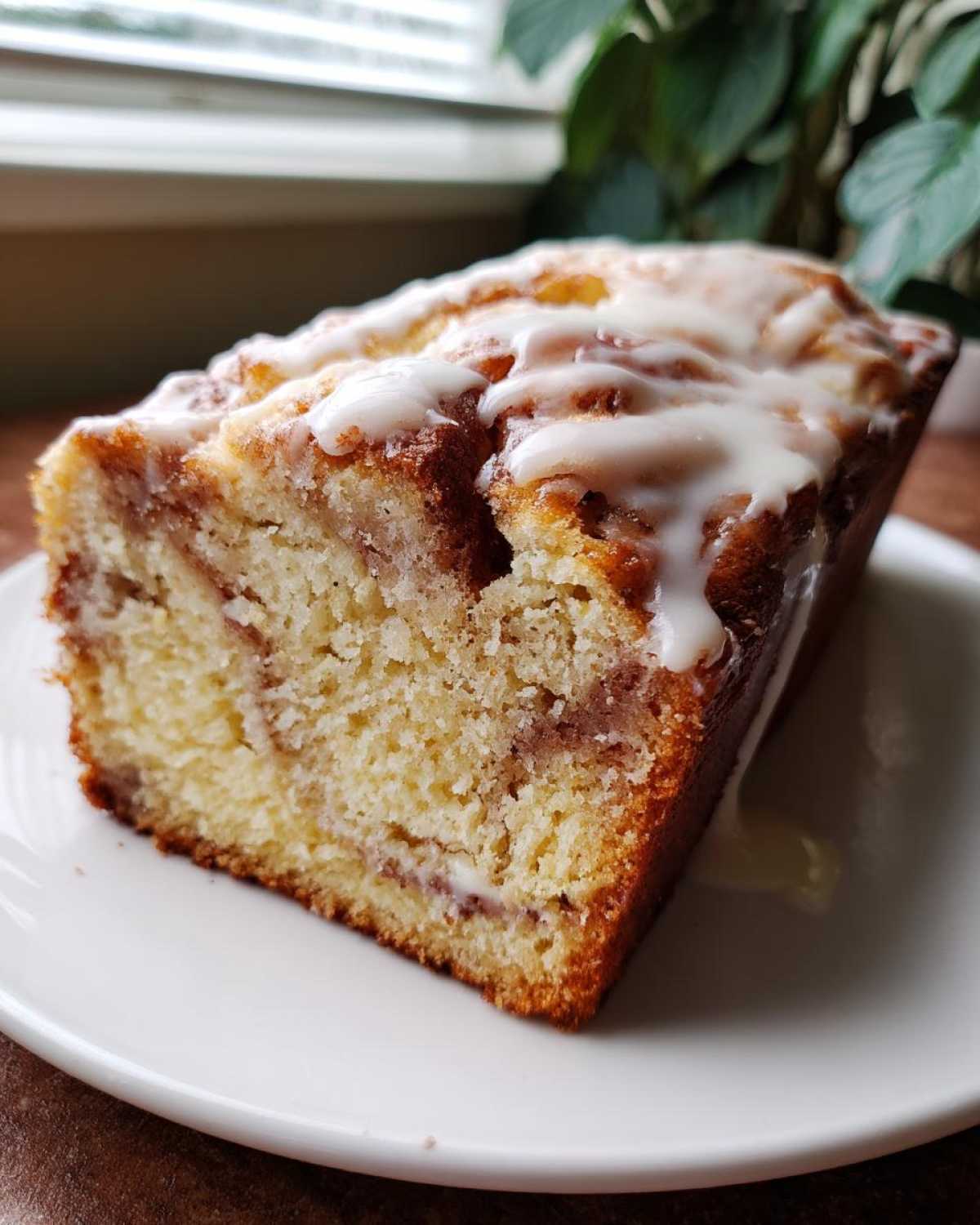 A close-up of a slice of moist apple fritter bread topped with a sweet white glaze, sitting on a white plate.