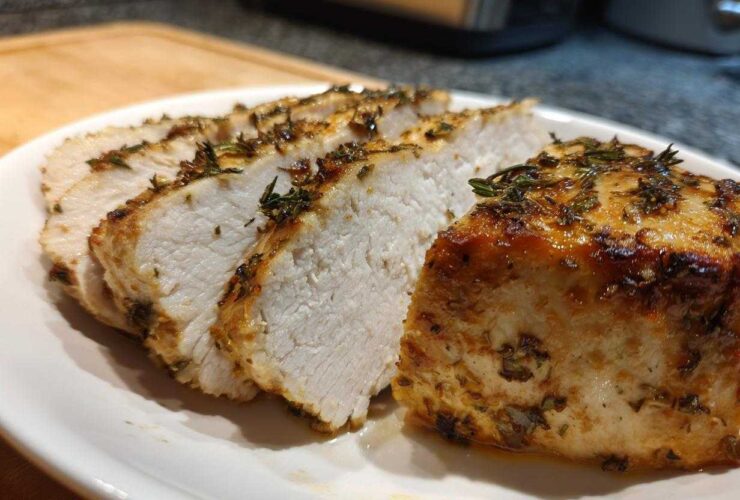 Close-up of juicy, sliced baked chicken breast seasoned with herbs on a white plate.