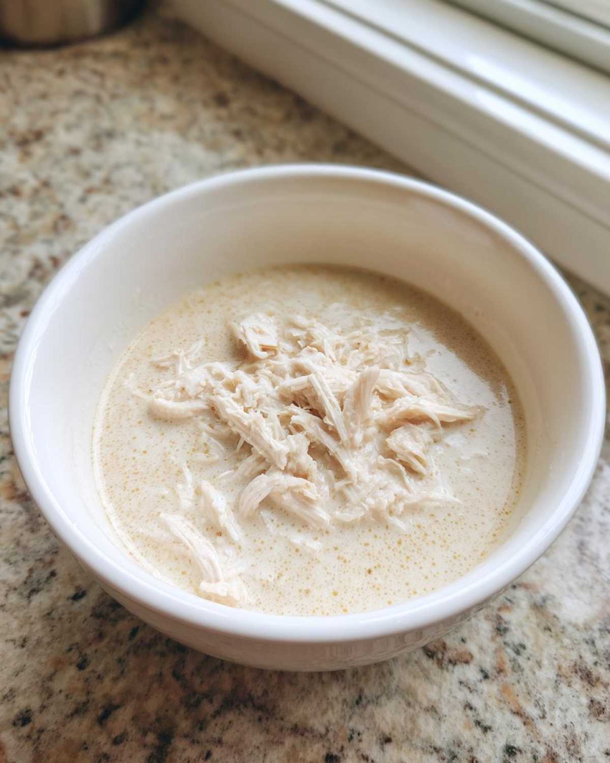 A white bowl filled with creamy soup topped generously with shredded chicken, representing cream of chicken soup.