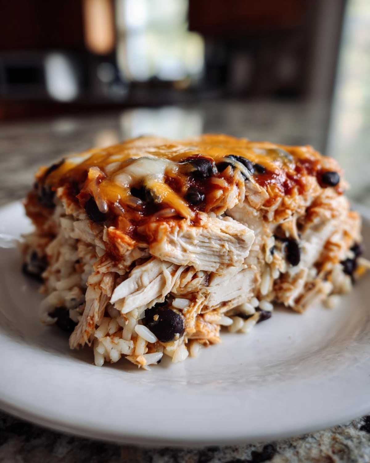 A generous serving of delicious burrito bake featuring shredded chicken, rice, black beans, and melted cheddar cheese.