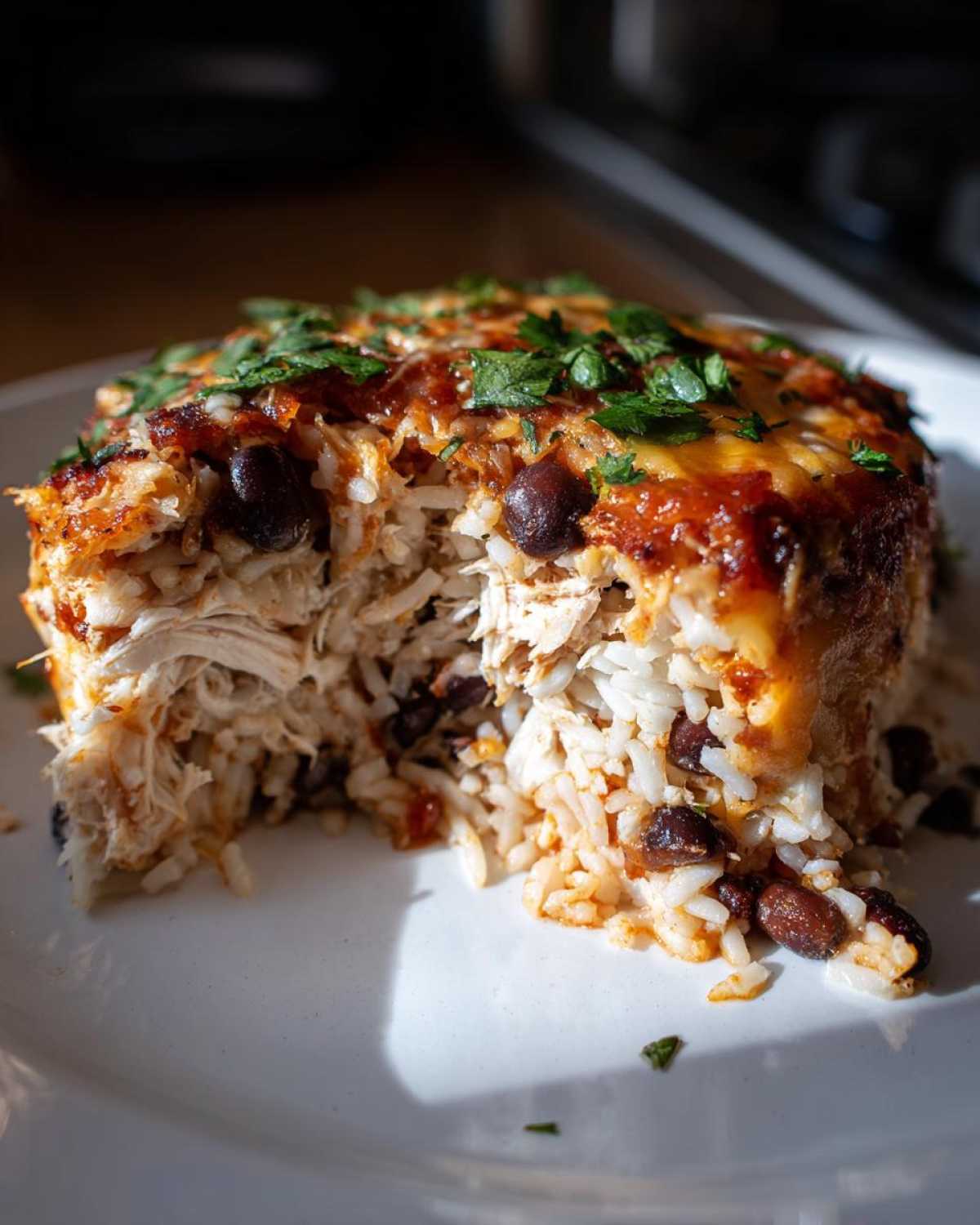 Close-up of a serving of burrito bake showing shredded chicken, rice, black beans, melted cheese, and cilantro garnish.
