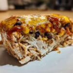 Close-up of a serving of burrito bake showing shredded chicken, rice, corn, black beans, and melted cheese topping.