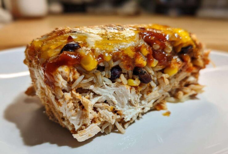 Close-up of a serving of burrito bake showing shredded chicken, rice, corn, black beans, and melted cheese topping.