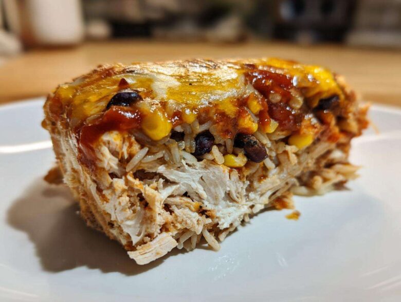 Close-up of a serving of burrito bake showing shredded chicken, rice, corn, black beans, and melted cheese topping.