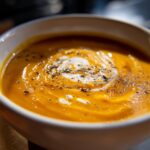 Close-up of a rich, orange butternut squash soup topped with a cream swirl and cracked black pepper.