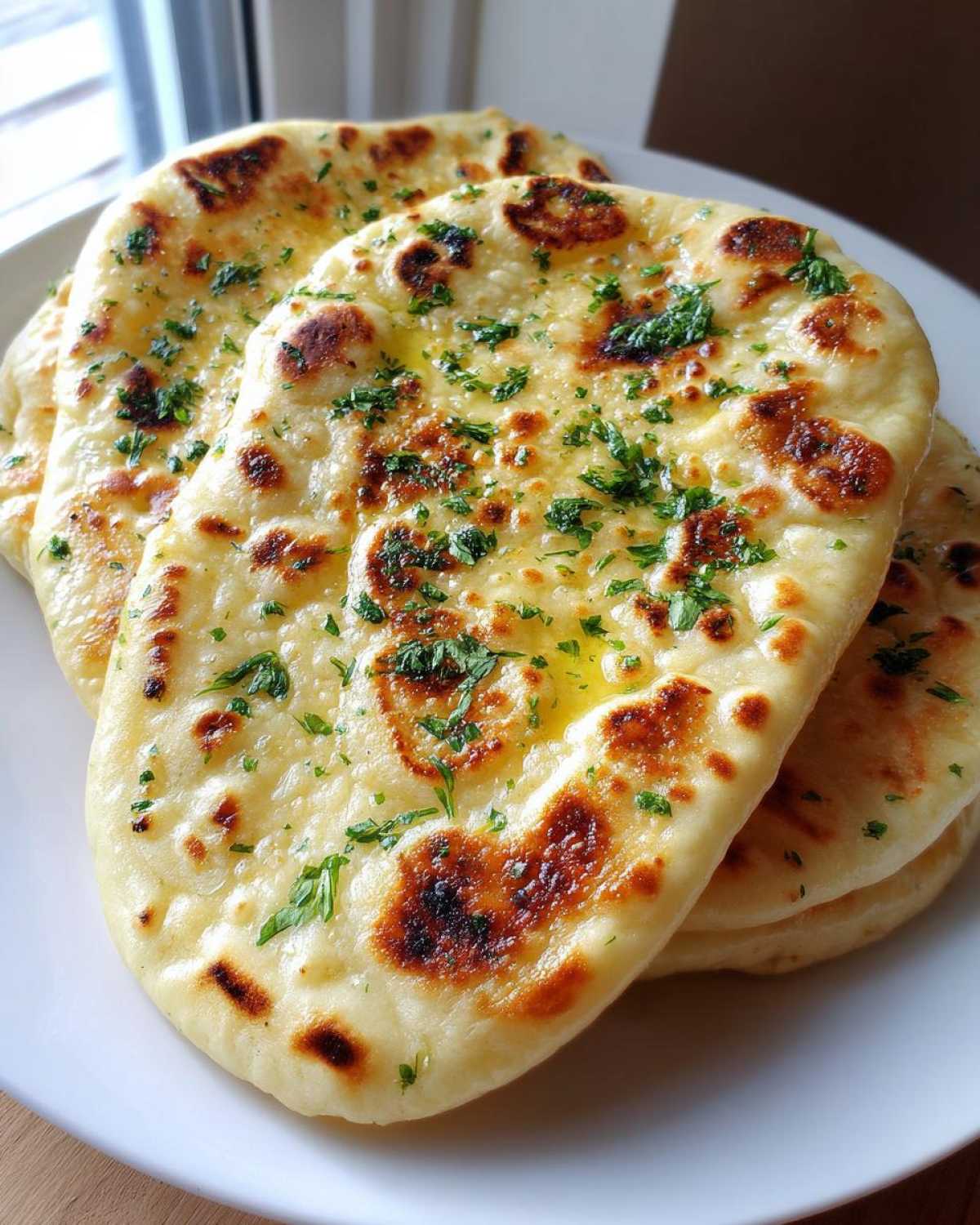 Close-up of freshly cooked, soft naan bread brushed with melted butter and sprinkled with fresh parsley.