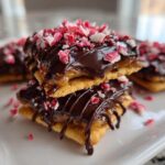 Two caramel ritz cracker christmas cookies stacked, drizzled with chocolate and topped with crushed peppermint.