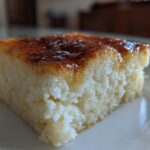 A close-up, side view of a square slice of moist cassava cake with a rich, caramelized brown topping.